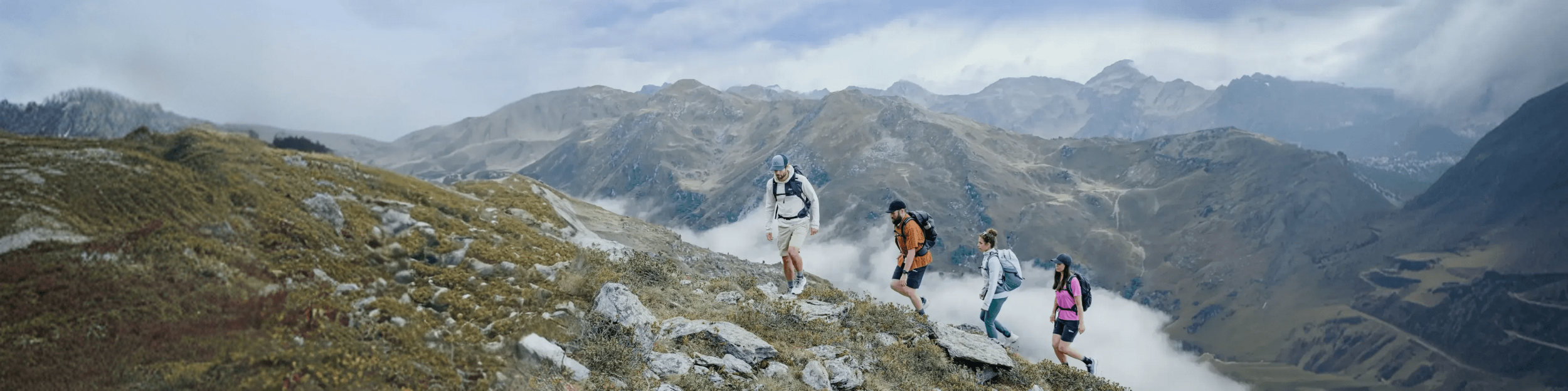 People hiking on a mountain trail with scenic mountains in the background