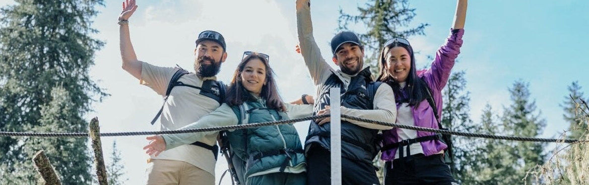 Four people standing on a wooden bridge with trees and blue sky in the background