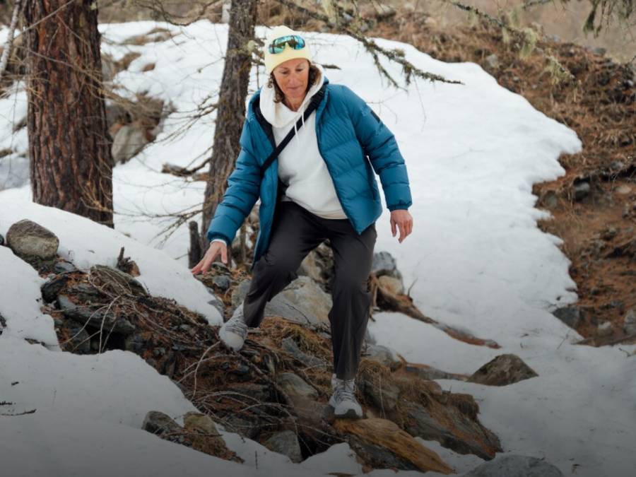 Two sleds with two people each are riding down a snowy slope. The people are laughing and wearing winter clothing, hats, and sunglasses; snow-covered mountains can be seen in the&nbsp;background.