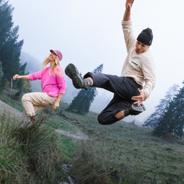 Two people are jumping on a green hill.